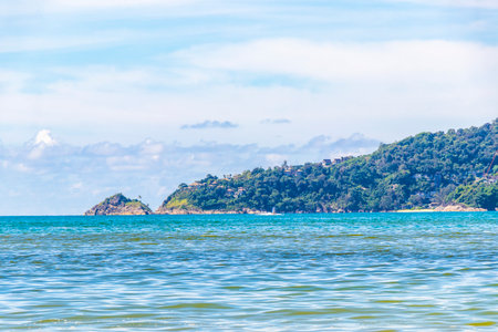 Beach bay sea coast panorama view with turquoise blue clear water waves and green mountains and palm trees.の写真素材
