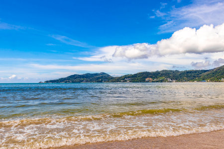 Patong Beach bay sea coast panorama view with turquoise blue clear water waves white sand and green mountains and palm trees in Patong Beach Kathu District Phuket Island Province Southern Thailand.の写真素材