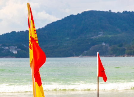 Kathu Phuket Thailand October 17, 2025 Patong Beach bay with red yellow flag warning sign sea coast panorama view turquoise blue clear water waves mountains in Patong Phuket Island Thailand.の写真素材