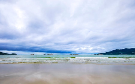 Patong Beach bay sea coast panorama view with turquoise blue clear water waves white sand and green mountains and palm trees.の写真素材