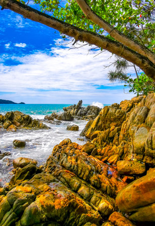 Amazing rocky Kalim Beach tropical landscape panorama view with blue sky turquoise water waves palm trees and rocks in Patong Beach Kathu Phuket Island Province Southern Thailand in Southeast Asia.の写真素材