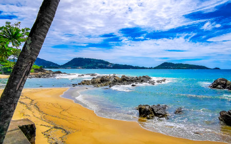 Amazing rocky Kalim Beach tropical landscape panorama view with blue sky turquoise water waves palm trees and rocks in Patong Beach Kathu Phuket Island Province Southern Thailand in Southeast Asia.の写真素材