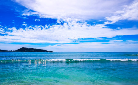 Kalim Beach bay sea coast panorama view with turquoise blue clear water waves white sand and green mountains and palm trees in Patong Beach Kathu Phuket Island Province Southern Thailand.の写真素材