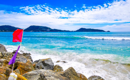 Amazing rocky Kalim Beach tropical landscape panorama view with blue sky turquoise water waves rocks and red pink and purple flag in Patong Beach Kathu Phuket Island Province Southern Thailand.の写真素材
