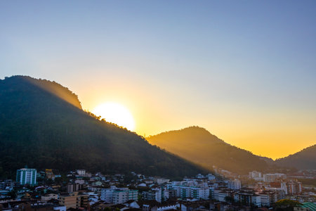 Beautiful golden colorful sunrise sunset behind the tropical mountain hill with city town panorama view.の写真素材