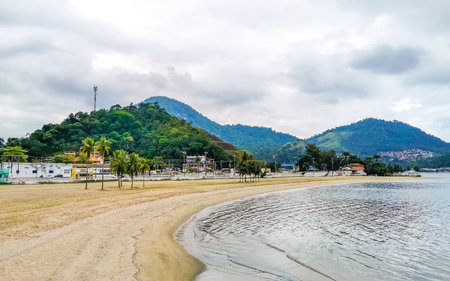Panorama of tropical Anil Beach with coastal shore seascape turquoise green clear water pier port harbor with boats blue sky and palm trees in Angra dos Reis State of Rio de Janeiro Brazil.の写真素材