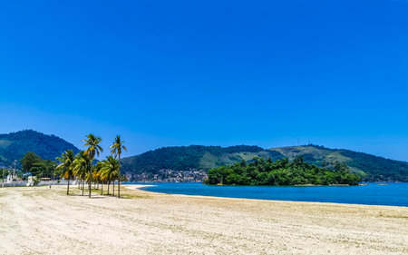 Panorama of tropical Anil Beach with coastal shore seascape turquoise green clear water pier port harbor with boats blue sky and palm trees in Angra dos Reis State of Rio de Janeiro Brazil.の写真素材