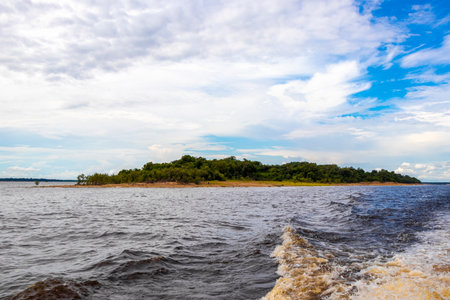 Meeting of waters blackwater of Rio Negro and whitewater of Amazon River boat trip tour with tropical jungle rainforest and blue cloudy sky in Iranduba Manaus State of Amazonas Brazil.の写真素材