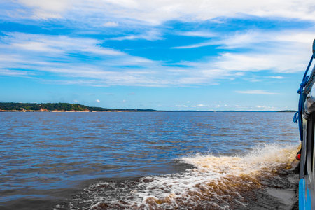 Meeting of waters blackwater of Rio Negro and whitewater of Amazon River boat trip tour with tropical jungle rainforest and blue cloudy sky in Iranduba Manaus State of Amazonas Brazil.の写真素材