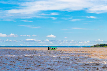 Meeting of waters blackwater of Rio Negro and whitewater of Amazon River boat trip tour with tropical jungle rainforest and blue cloudy sky in Iranduba Manaus State of Amazonas.の写真素材
