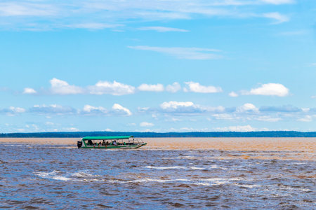 Meeting of waters blackwater of Rio Negro and whitewater of Amazon River boat trip tour with tropical jungle rainforest and blue cloudy sky in Iranduba Manaus State of Amazonas Brazil.の写真素材