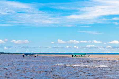 Meeting of waters blackwater of Rio Negro and whitewater of Amazon River boat trip tour with tropical jungle rainforest and blue cloudy sky in Iranduba Manaus State of Amazonas Brazil.の写真素材