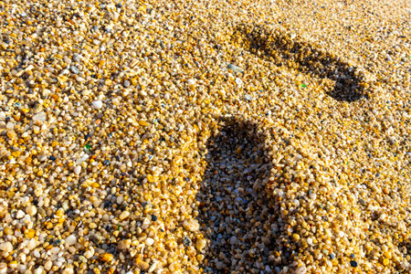 Beach sand with pebbles stones rocks colorful shells mussels and footprint footprints texture pattern in Patong Kalim Beach Kathu District Phuket Island Province Southern Thailand.の写真素材