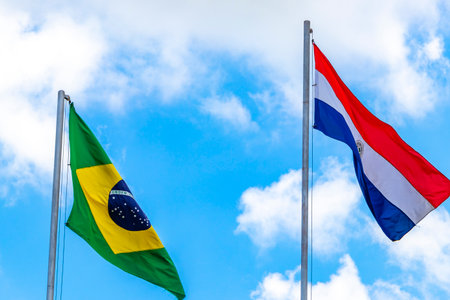 Brazilian and Paraguayan flags waving in the wind with blue sky in the background in Foz do Iguacu State of Parana Brazil.の写真素材