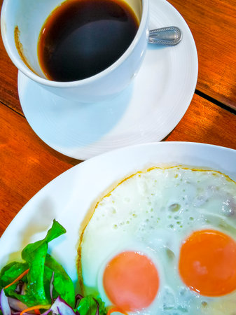 Breakfast with sausages, toast, eggs, salad, bacon, and a cup of coffee on a plate in a restaurant in Patong Beach, Kathu District, Phuket Island, Southern Thailand.の写真素材
