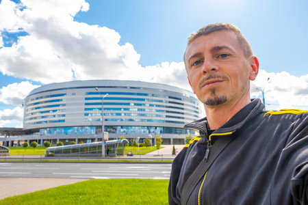 Man tourist takes selfie photo in front of the modern Minsk Arena in the city with big screen in the...