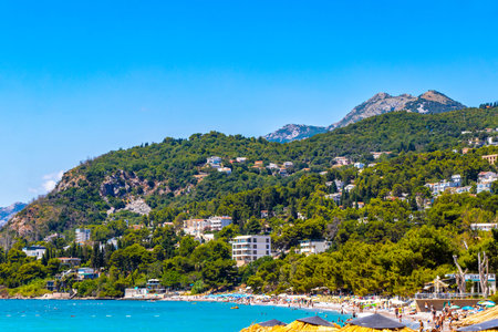 Susanj Bar Municipality Montenegro 25. July 2025 Miejska and Chico Rico Beach bay tourists people water waves sun loungers parasols tropical plants blue sky and palm trees in Susanj Bar Montenegro.のeditorial素材