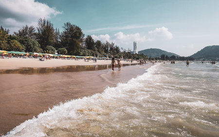 Kathu District Phuket Island Province Thailand 04. March 2026 Patong Kamala Beach bay with tourists people water waves sun loungers parasols tropical plants blue sky and palm trees in Phuket Thailand.のeditorial素材