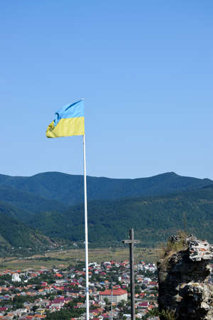 Ukraine flag and christian cross with panorama of Khust city background. View from ruin of old castle. Landscape, Zakarpattia Oblast. Ukraine.の写真素材