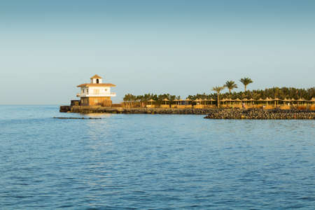 Cape with wattled umbrellas, palm trees and a house in the evening.の写真素材