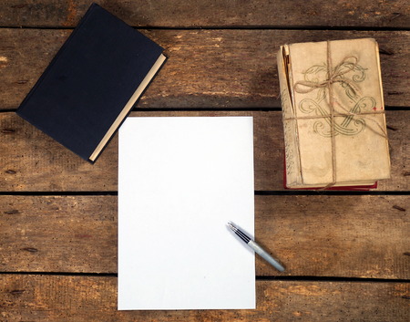 Aged books and white paper on wooden tableの写真素材