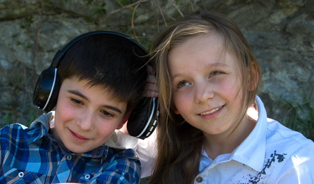 Little boy listens music with earphones and litle girl tryes to hear what does he leaten toの写真素材