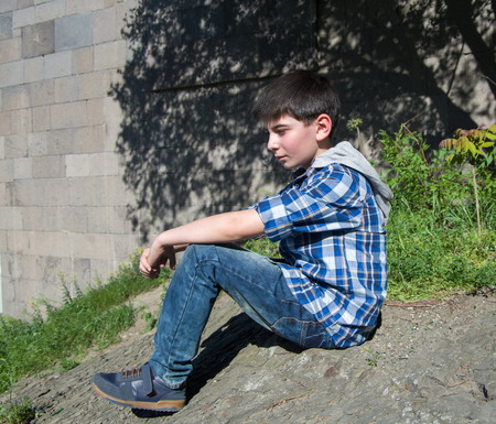 Teenage boy sits on a clif in a city park areaの写真素材