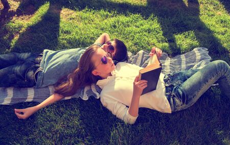 Little teenage boy and girl are lying on grass, girl reads book and boy wears earphones chilloutの写真素材