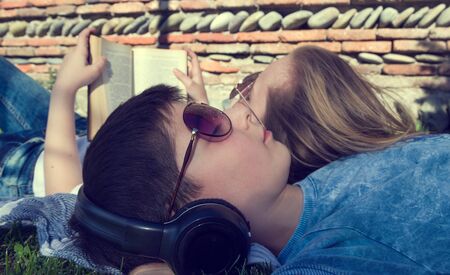 Little teenage boy and girl are lying on grass, girl reads book and boy wears earphones chilloutの写真素材