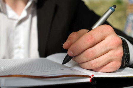 Left handed businessman is writing something in a notebookの写真素材