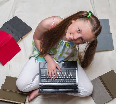 A little girl is studying with laptop and books around her top viewの写真素材