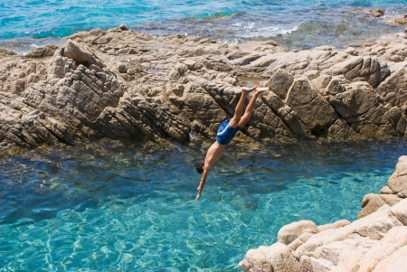 Plunge of a young boy from a cliff in a beautiful blue seaの写真素材
