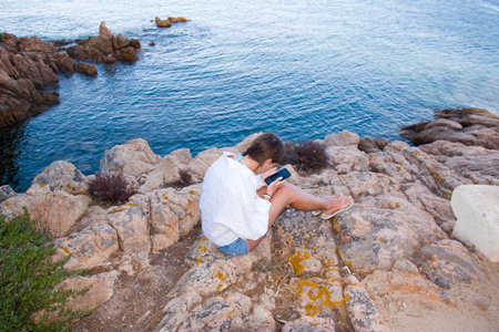 Girl alone with her phone on the rocksの写真素材