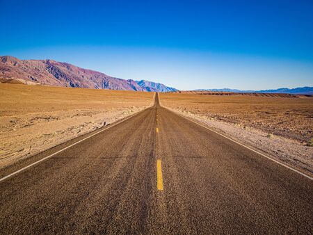 The lane of endless straight Badwater Road running through the barren scenery of famous Death...