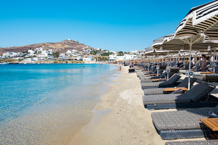 Mikonos, Greece - 12 Aug 2023: Ornos Beach. With umbrella and luxury beach chairs beds in front of blue ocean, Ornos is a family beach with crystal and shallow water.のeditorial素材