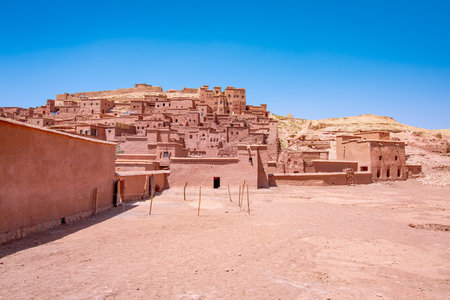 Traditional Moroccan earthen architecture rising on a hill under a clear blue sky, showcasing the picturesque Ait Benhaddou Kasbah and its rich historical significanceの写真素材