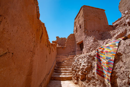 Colorful carpets hanging against a red wall in the ancient Ait Benhaddou Kasbah highlight the vibrant culture and unique architecture of Moroccos UNESCO siteの写真素材
