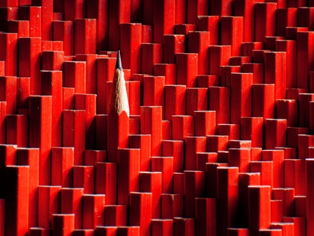 A red graphite pencil sticking out of a large group of blunt pencils.