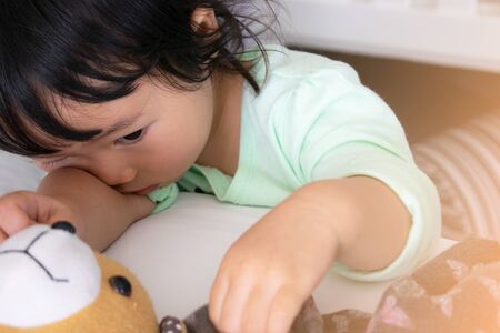 Asian girl hug her doll and cry or scare or sad or feel bad or in trouble.Sitting on the bed.Selective focus.Concept of orphan kid.の写真素材