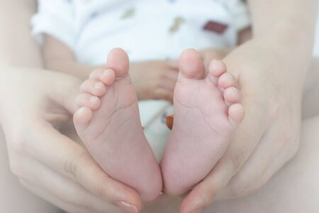 Baby feet in mother hands. Tiny Newborn Baby's feet on female Shaped hands closeup. Mom and her Child. Happy Family concept. Beautiful conceptual image of Maternityの写真素材