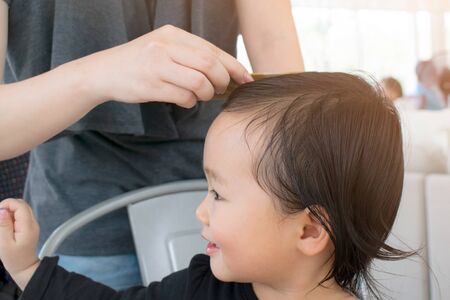 My daughter. Beautiful happy mother smiling and making a hairdo for her little daughter while standing behind her childの写真素材