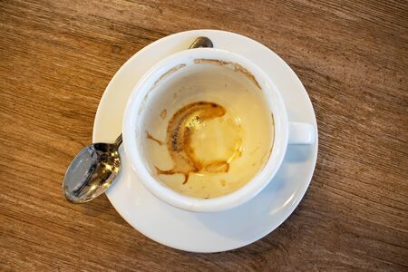 A cup of coffee that has been used empty on a saucer that is covered with many stains on the wood background. Top viewの写真素材