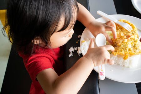 A child is trying to eat with spoon and fork by herself. Baby eating.の写真素材