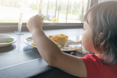 A child is trying to eat with spoon and fork by herself. Baby eating.の写真素材