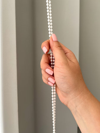 A female hand holding a beaded chain for the blinds