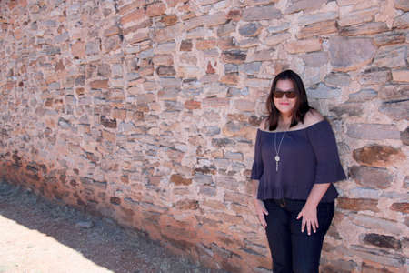 Latin adult woman with sunglasses and stone wall background relaxed and happy enjoying the sunny dayの写真素材