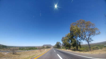 Empty straight road surrounded by trees with the sun in front seen from the car on a road trip, time to rest and relaxの写真素材