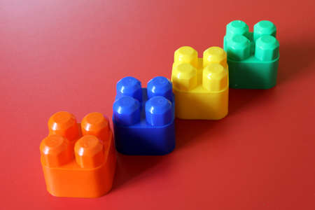 Buildable colored plastic blocks to play, build and organize on a red background as a concept of...