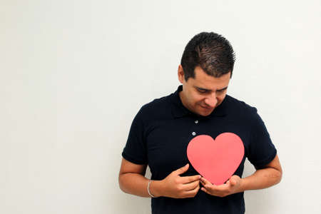Latin adult man shows a big red heart for his enthusiasm for the arrival of February and celebrate Valentine's Day of Love and Friendship with his family, friends and partner with happiness and affectの写真素材