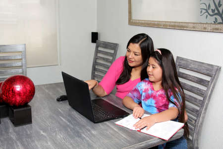 Hispanic Mom and Daughter Home School with Homework in New Normal Due to Covid-19 Pandemicの写真素材